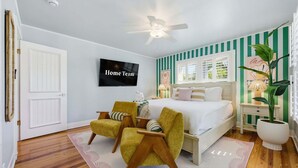 Ein Schlafzimmer mit einem Bett, zwei Stühlen, einem Fernseher und einem Deckenventilator.