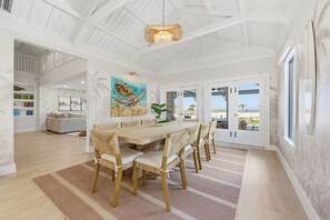 A spacious dining area with a long wooden table and chairs, a large painting of a sea turtle, and a view of the ocean through large sliding doors. - Award-winning Private Beach Breathtaking Sunsets (Clearwater Beach)