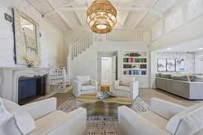 A spacious living room with a fireplace, white sofas, a coffee table, and a staircase leading to an upper level. - Award-winning Private Beach Breathtaking Sunsets (Clearwater Beach)