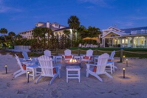A beachfront property with a fire pit surrounded by Adirondack chairs, a covered outdoor area, and a large building with multiple windows. - Award-winning Private Beach Breathtaking Sunsets (Clearwater Beach)