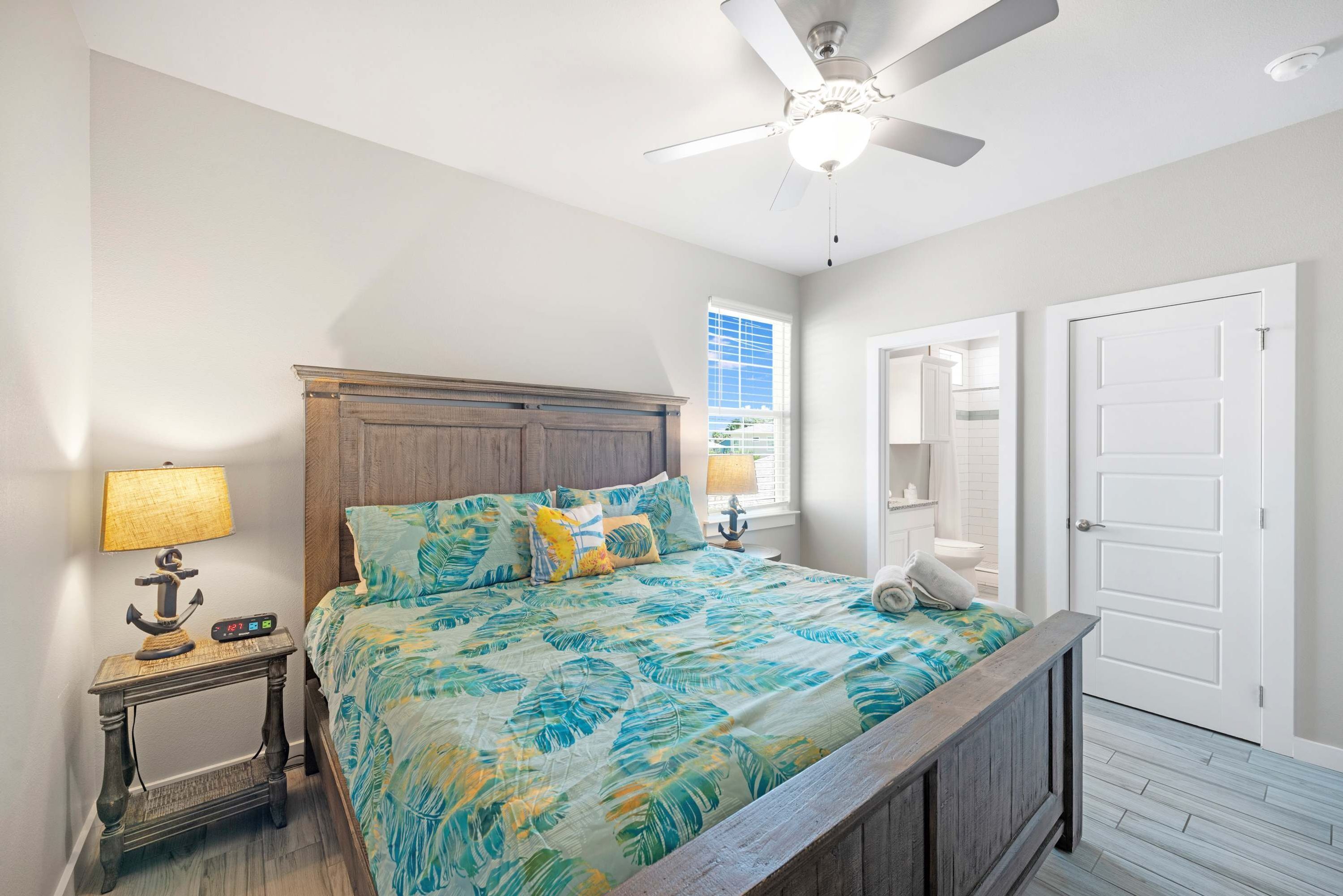 A bedroom with a bed, a nightstand, a ceiling fan, a window, and a door.