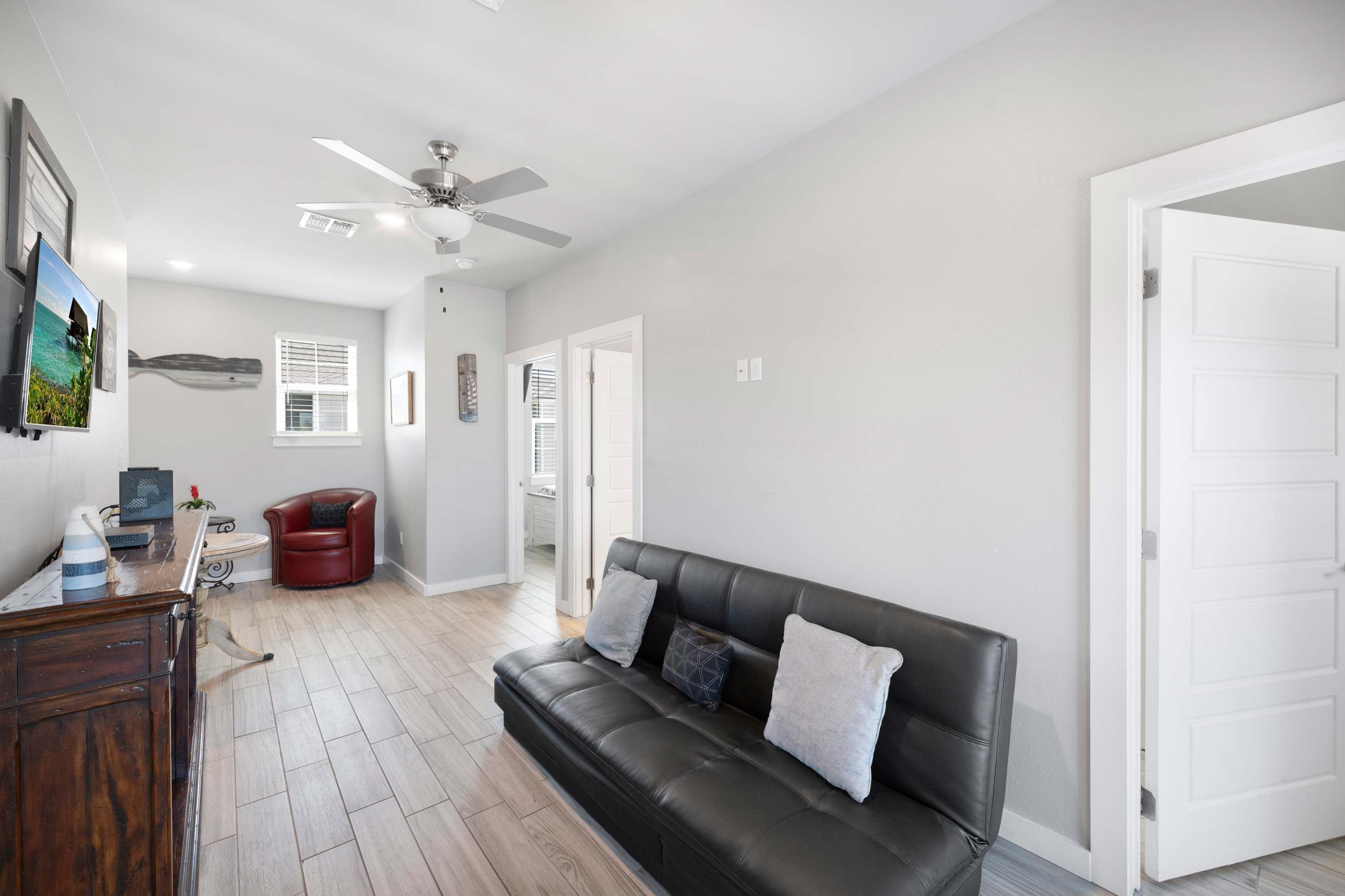 A spacious living room with a black leather sofa, a wooden coffee table, and a ceiling fan.