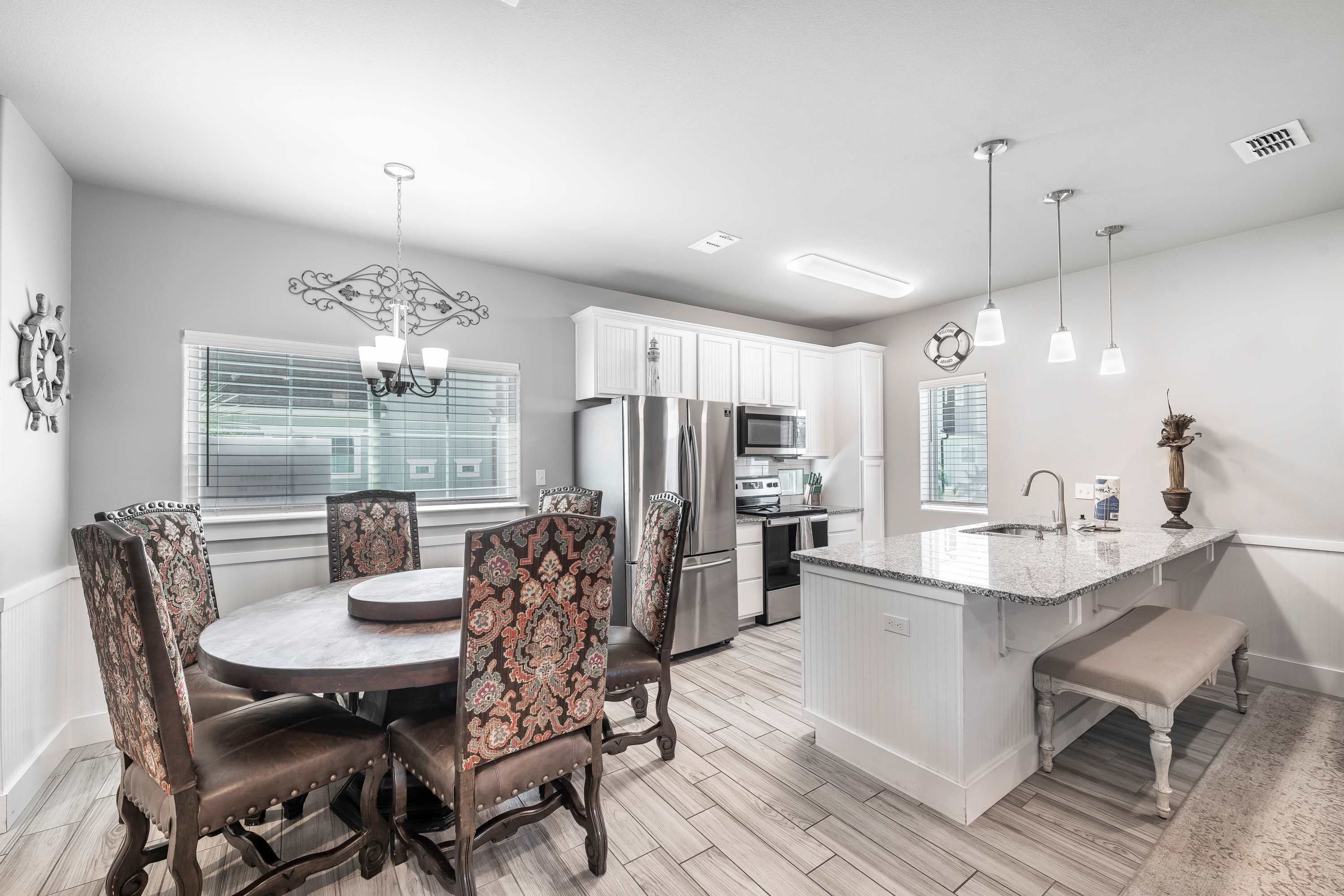 A modern kitchen with a central island, white cabinetry, and a dining area with patterned chairs.