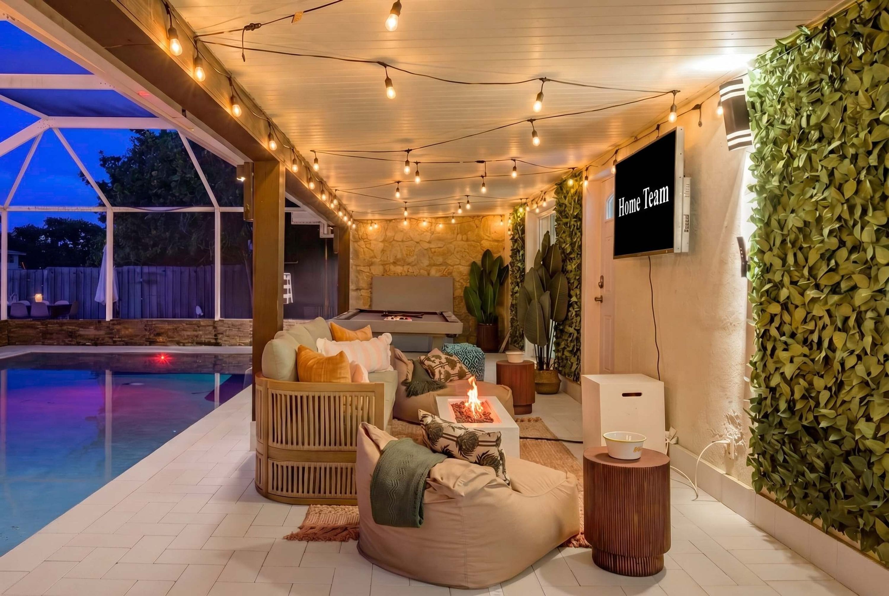 A cozy outdoor seating area with a fire feature, a pool, and a wall-mounted television.