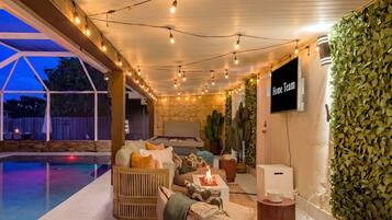 A cozy outdoor seating area with a fire feature, a pool, and a wall-mounted television.