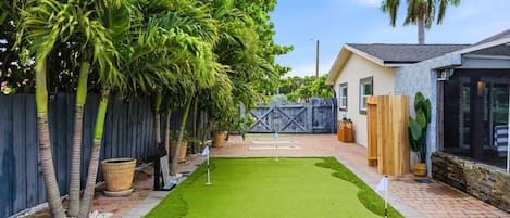 A backyard with artificial grass, a wooden fence, and a palm tree.