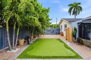 Un patio con césped artificial, cerca de madera y una palmera.