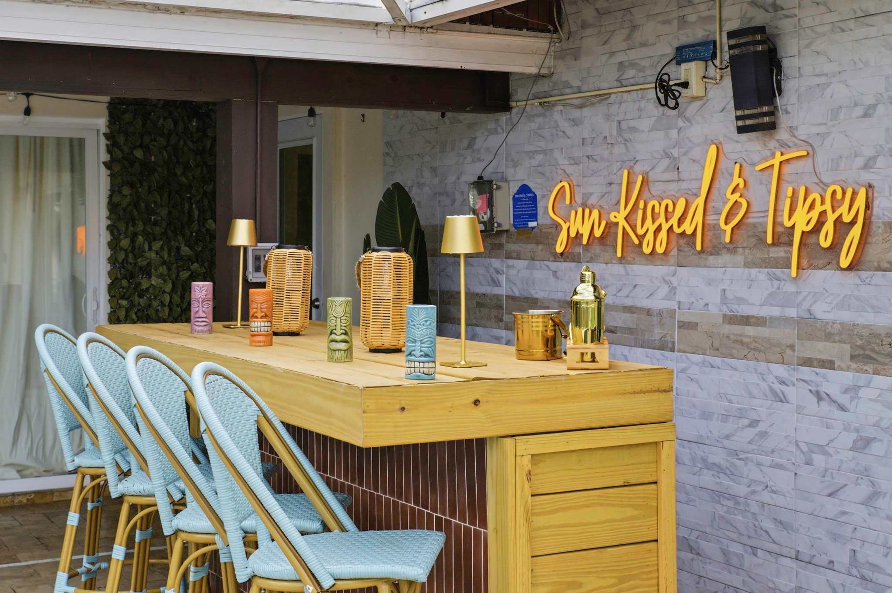 Un espace bar agrémenté d’un néon, de chaises en osier et de tabourets de bar.