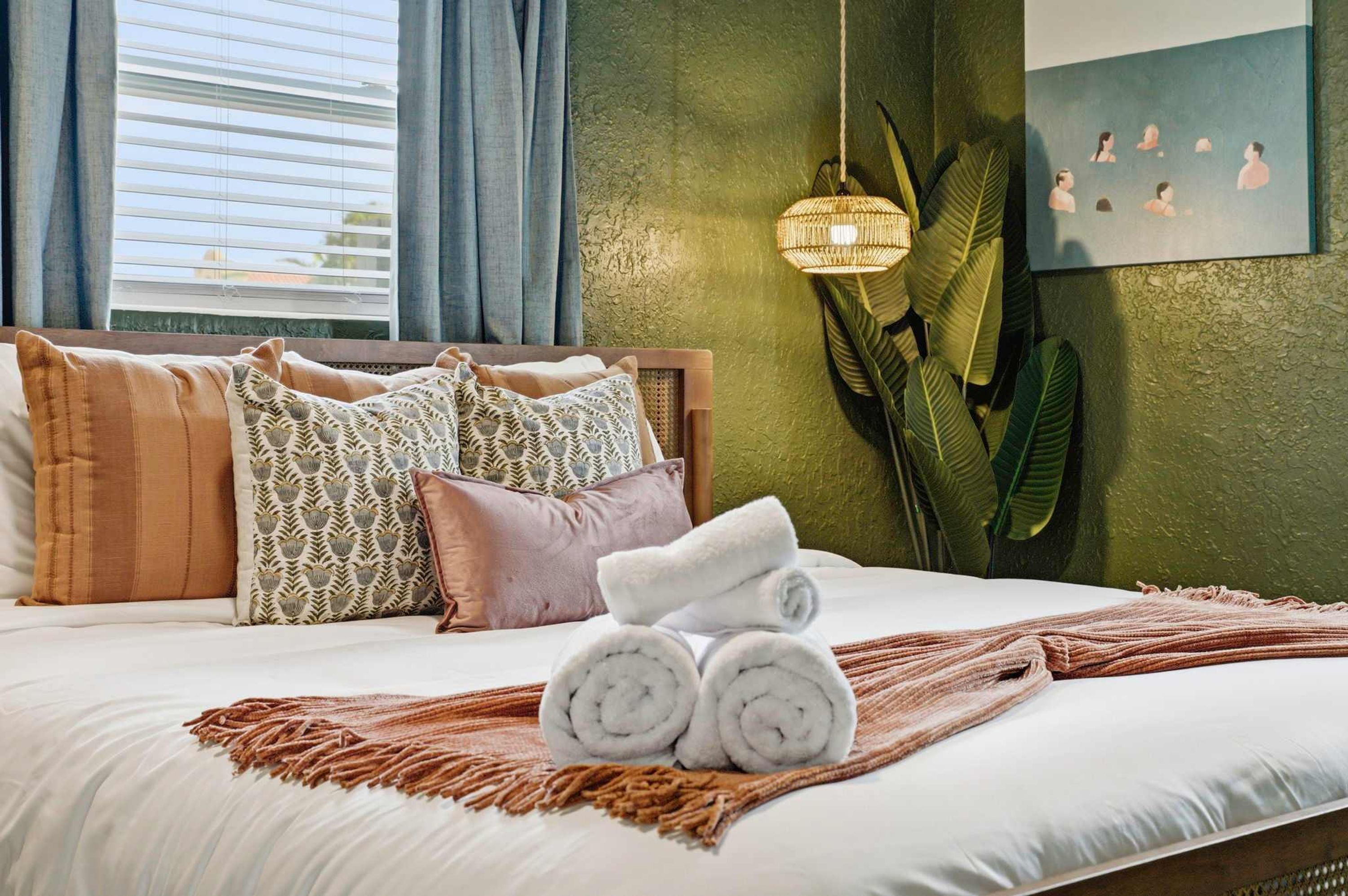 A neatly made bed with rolled towels, patterned pillows, and a woven throw.