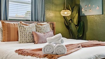 A neatly made bed with rolled towels, patterned pillows, and a woven throw.