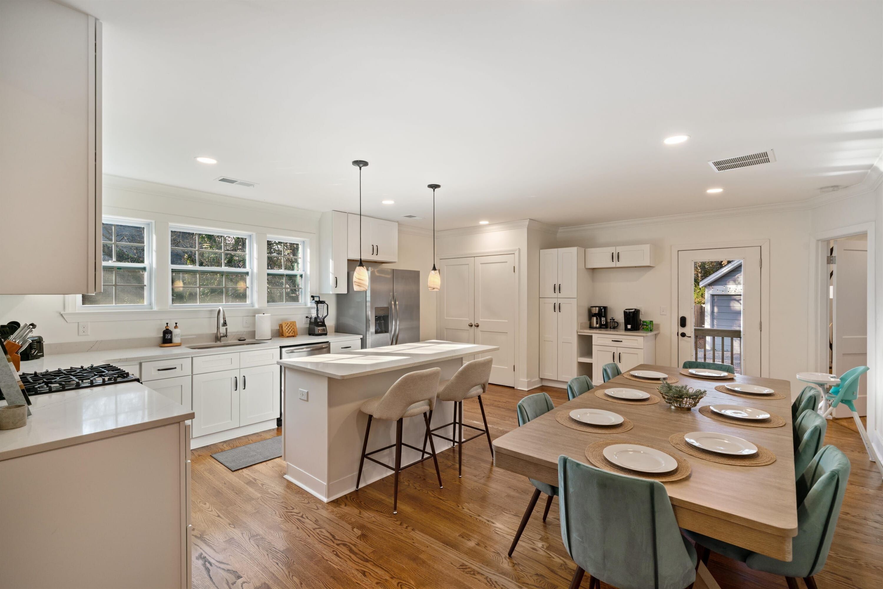 A modern kitchen with white cabinetry, a central island, and a dining area with a wooden table and chairs.