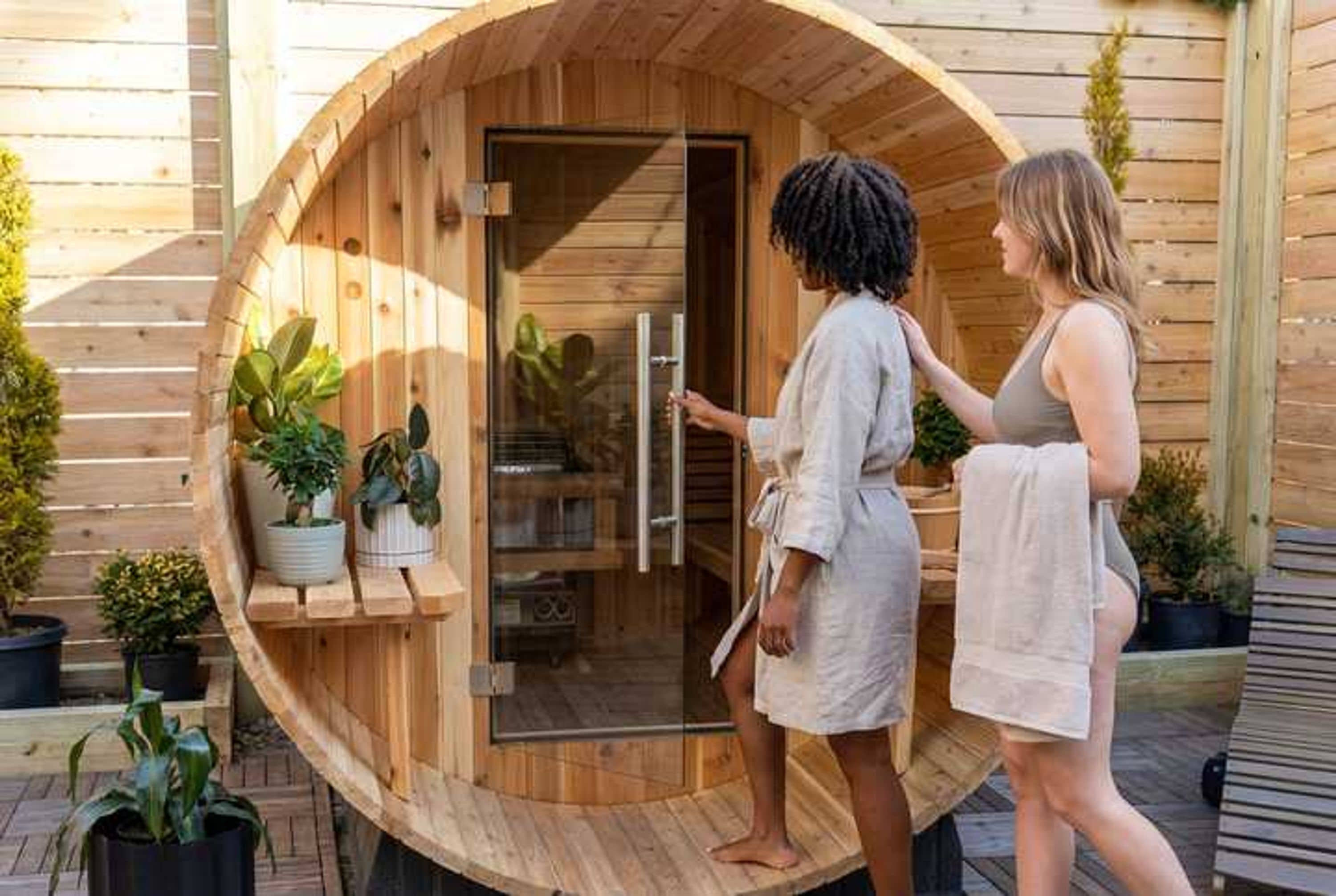 A wooden sauna with a glass door, surrounded by potted plants.