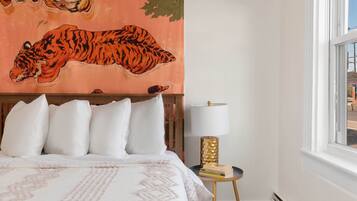 A bedroom with a bed, pillows, a wall tapestry of a tiger, a lamp, and a window.
