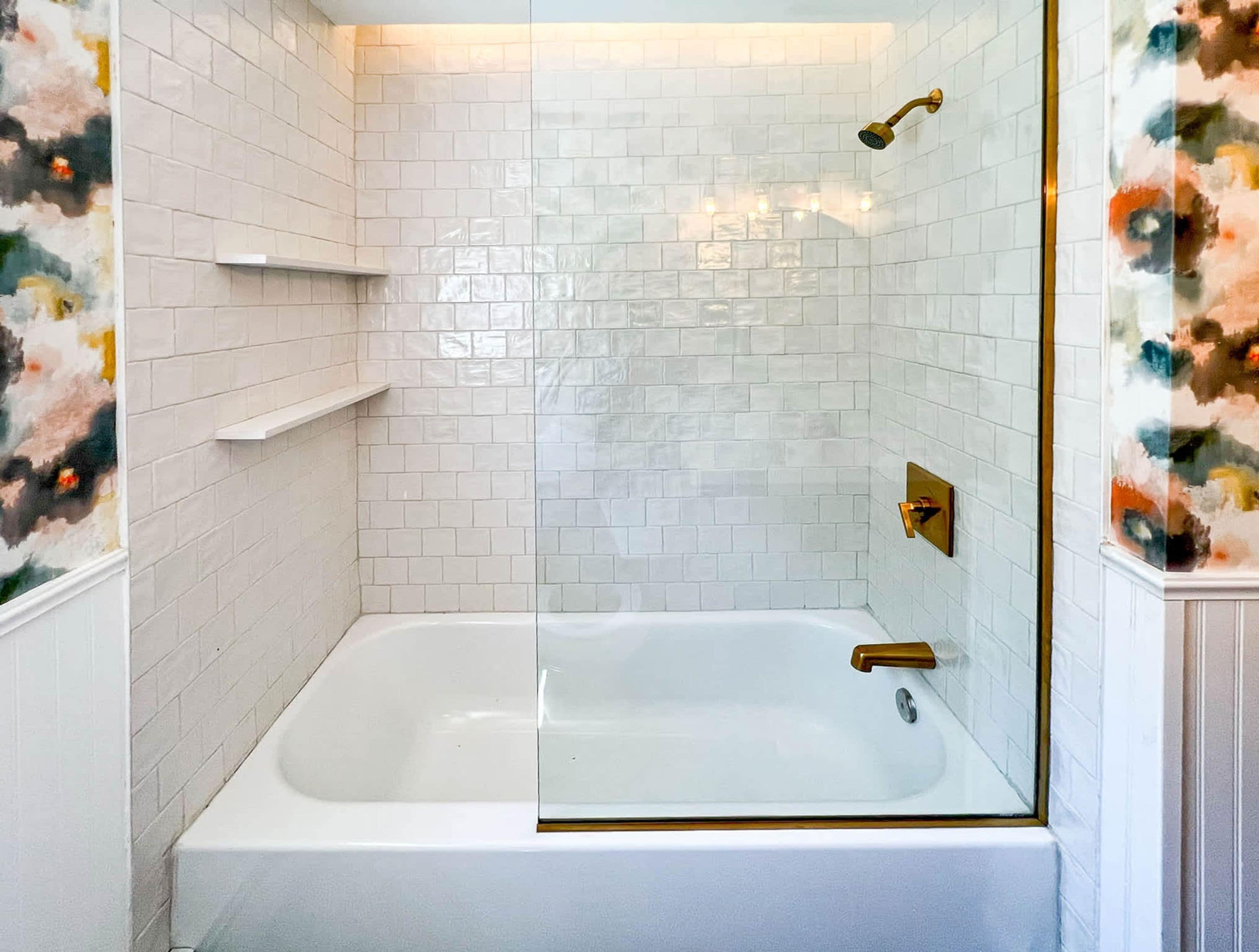 Une salle de bain avec une baignoire blanche, une douche à parois de verre et un mur recouvert de carreaux blancs.