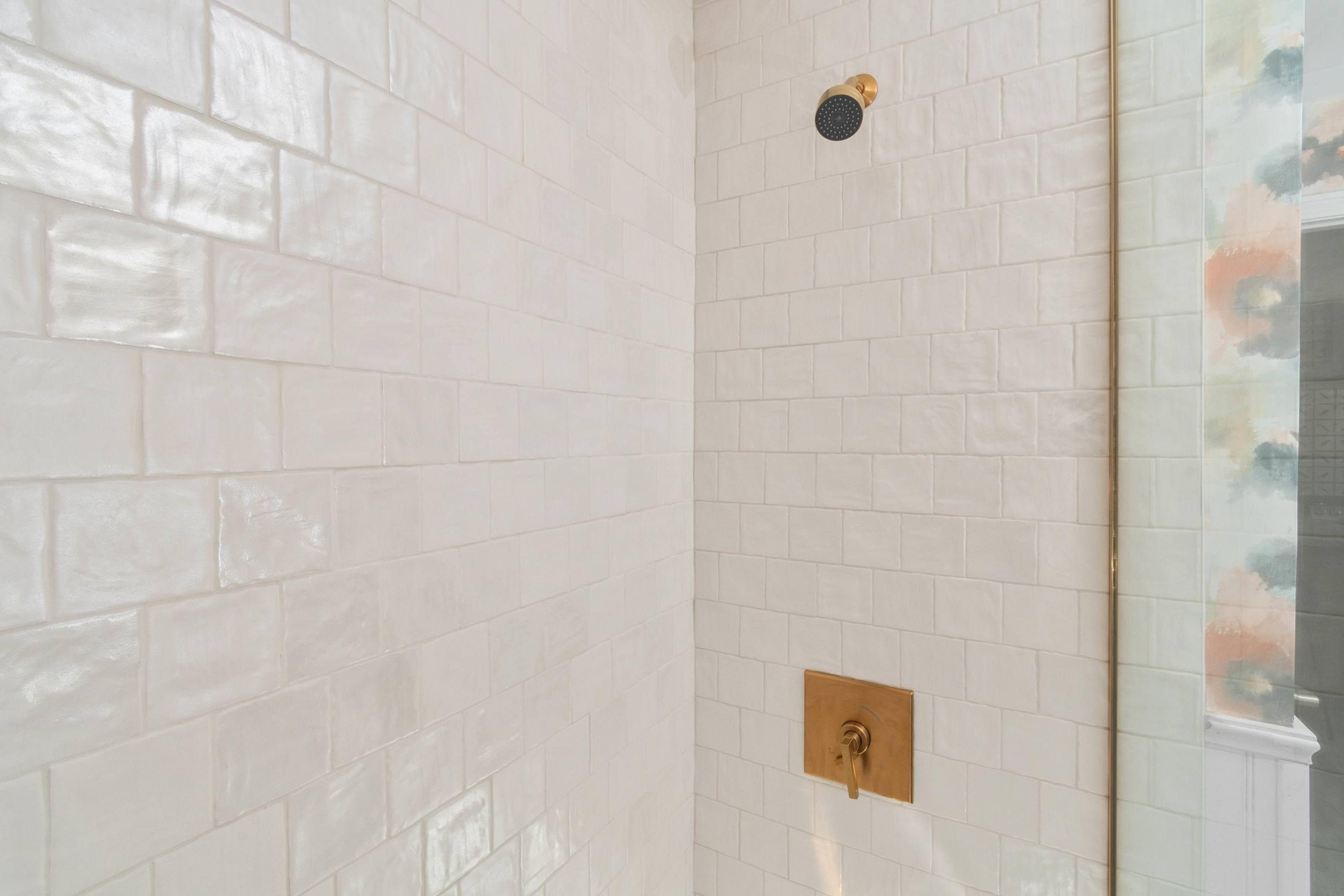 Une salle de bain avec des carreaux de céramique blancs rectangulaires, un robinet de douche doré et une porte de douche en verre.