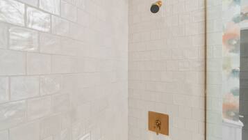 Une salle de bain avec des carreaux de céramique blancs rectangulaires, un robinet de douche doré et une porte de douche en verre.