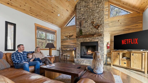 A cozy living room with a stone fireplace, leather sofas, and a television displaying the Netflix logo. - Mountain View Hot Tub Sauna Fire Pit (Blue Ridge)