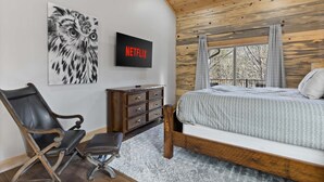 A bedroom with a bed, a chair, a dresser, a wall-mounted TV, and a painting of an owl. - Mountain View Hot Tub Sauna Fire Pit (Blue Ridge)