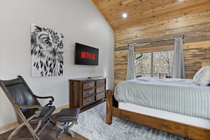 Quarto com cama, uma cadeira, cômoda, televisão na parede e um quadro de uma coruja.