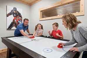 Uma família jogando pebolim em uma mesa de madeira com superfície de jogo branca.