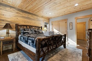 A bedroom with a wooden bed frame, a nightstand, a lamp, and a view of the outside. - Mountain View Hot Tub Sauna Fire Pit (Blue Ridge)