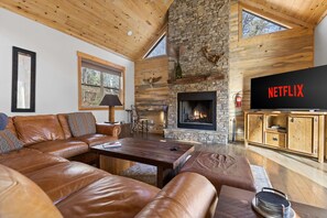 A cozy living room with a stone fireplace, leather sofa, and a television displaying 'NETFLIX'. - Mountain View Hot Tub Sauna Fire Pit (Blue Ridge)