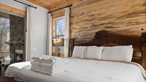 A bedroom with a wooden headboard, a fireplace, and a window with curtains. - Mountain View Hot Tub Sauna Fire Pit (Blue Ridge)