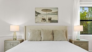 A bedroom with a large bed, two bedside tables with lamps, a headboard, and a beach-themed painting on the wall. - Bradenton Beachfront Pool Game Room (Bradenton)