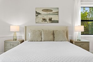 A bedroom with a large bed, two bedside tables with lamps, a headboard, and a beach-themed painting on the wall. - Bradenton Beachfront Pool Game Room (Bradenton)