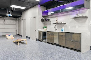 A kitchen area with a sink, cabinets, and a small plant. - Bradenton Beachfront Pool Game Room (Bradenton)