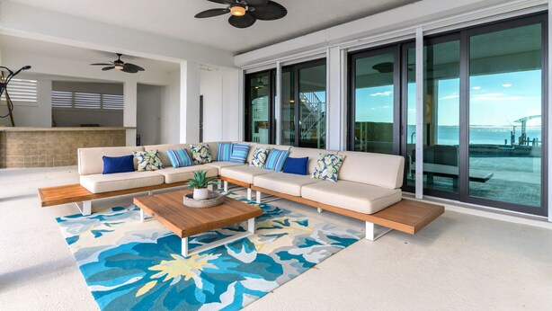 A modern living room with a sectional sofa, a coffee table, and a large window offering a view of the outdoors. - Bradenton Beachfront Pool Game Room (Bradenton)