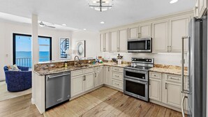 A modern kitchen with stainless steel appliances, white cabinetry, and a large island with a granite countertop. - Bradenton Beachfront Pool Game Room (Bradenton)