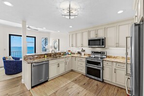 A modern kitchen with stainless steel appliances, white cabinetry, and a large island with a granite countertop. - Bradenton Beachfront Pool Game Room (Bradenton)