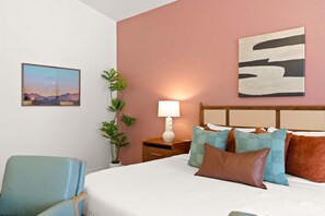 Ein Hotelzimmer mit einem Bett, einem Nachttisch, einer Lampe, einem Sessel und einem Wandbild.