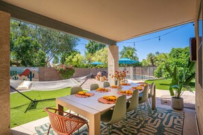 An outdoor patio with a table set for dining, surrounded by chairs, a hammock, and a pool area. - Desert Daze A Fun-filled 5BR Retreat Sleeps 12 (Mesa)