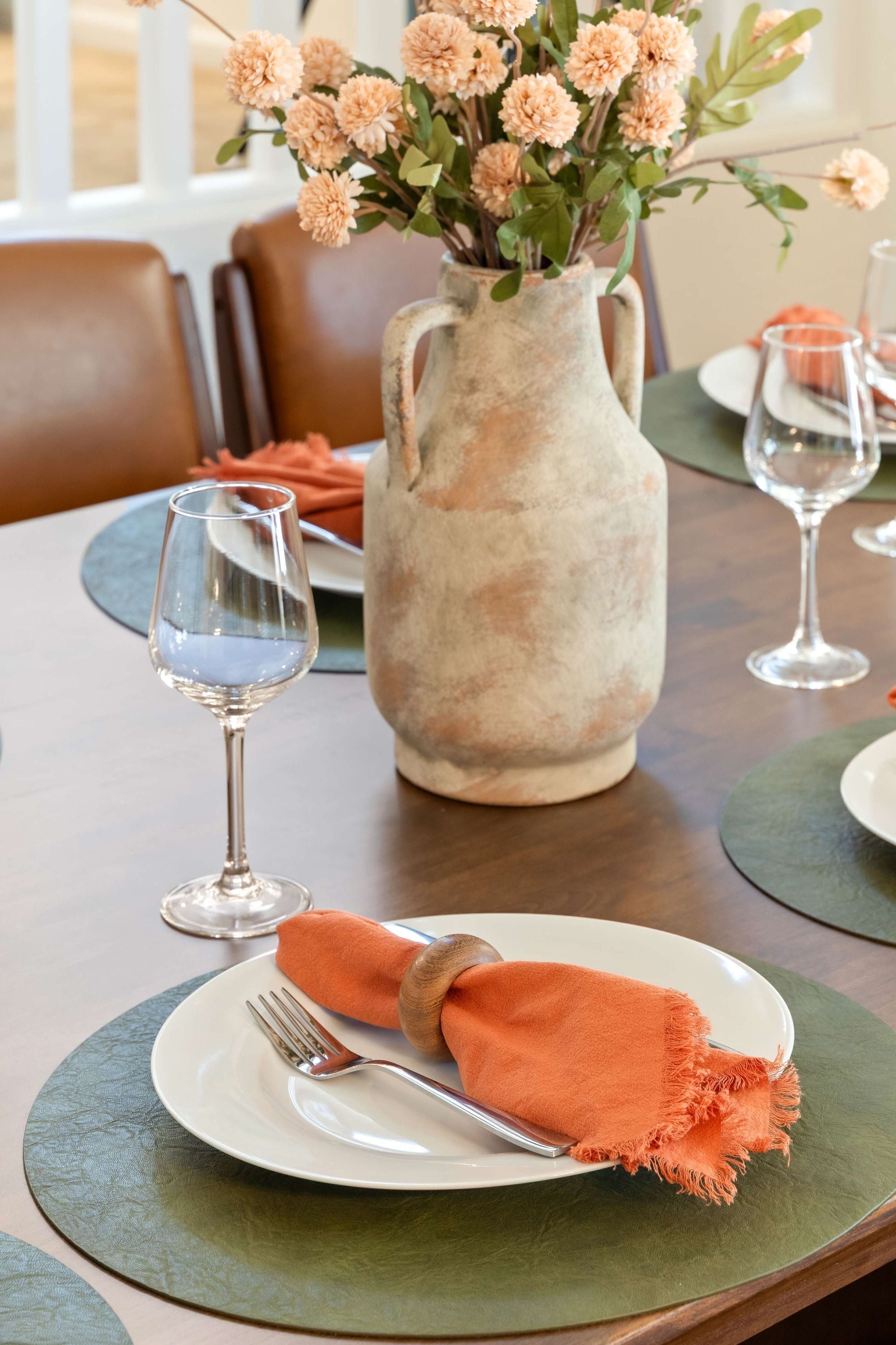 A dining table set with plates, cutlery, and a vase with flowers.