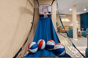 Ein Basketballkorb mit einem 'POPA-SHOT'-Schild, eine blaue Rutsche und vier Basketballsäcke unten.