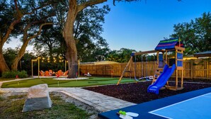 A backyard with a wooden play structure, a blue slide, and a small patio area with a table and chairs. - Resort-style Oasis Pool Mini Golf Playground (Largo)
