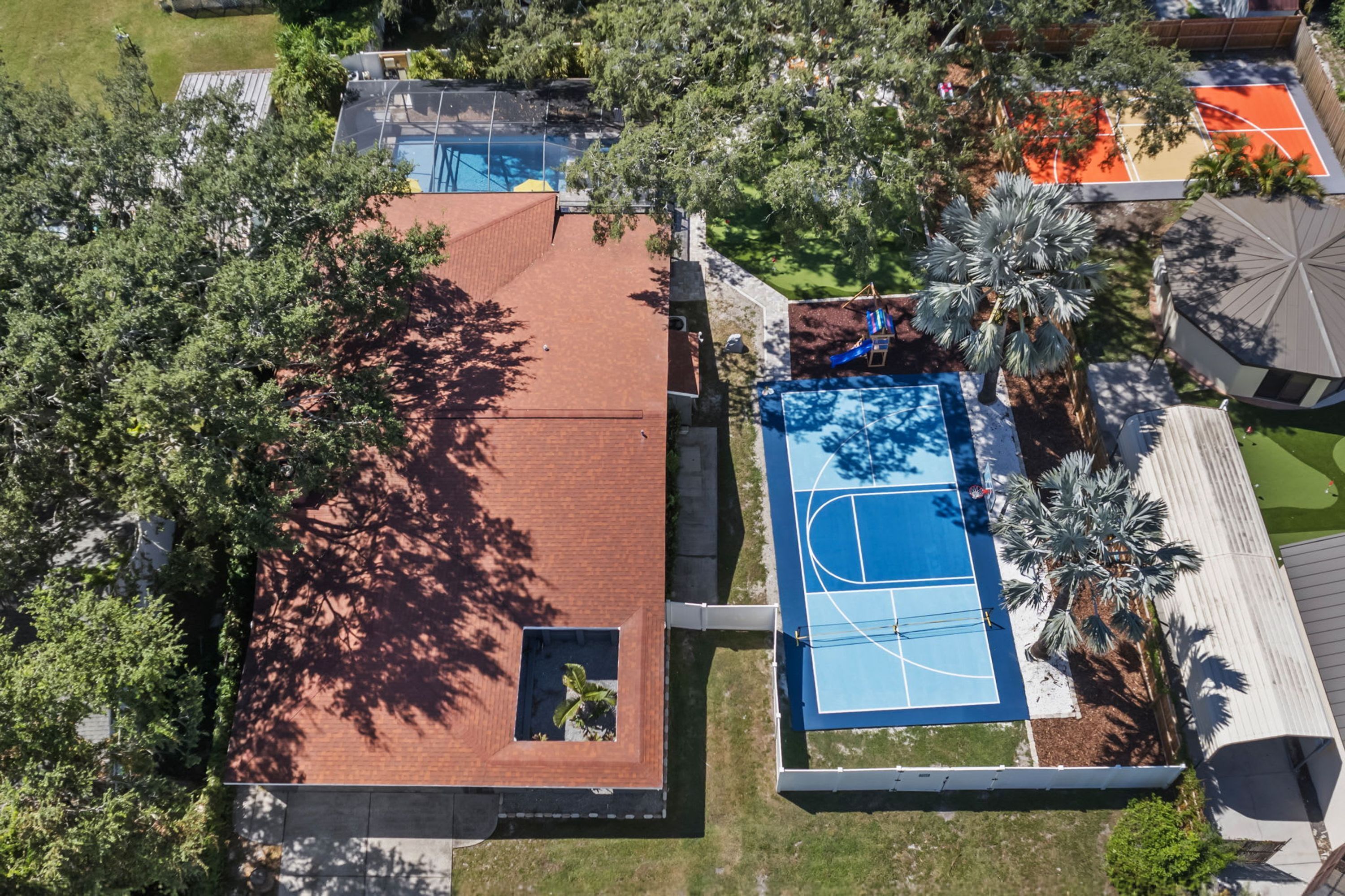 Vue aérienne d’un quartier résidentiel avec une piscine, un court de tennis et un patio couvert.