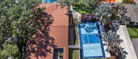 Vue aérienne d’un quartier résidentiel avec une piscine, un court de tennis et un patio couvert.
