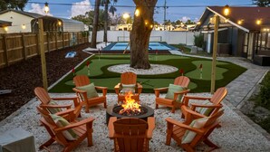 A backyard with a fire pit surrounded by Adirondack chairs, a small putting green, and a tree. - Resort-style Oasis Pool Mini Golf Playground (Largo)