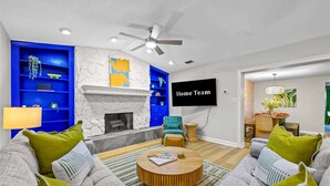 A modern living room with a fireplace, blue shelving, a television, and a ceiling fan. - Resort-style Oasis Pool Mini Golf Playground (Largo)