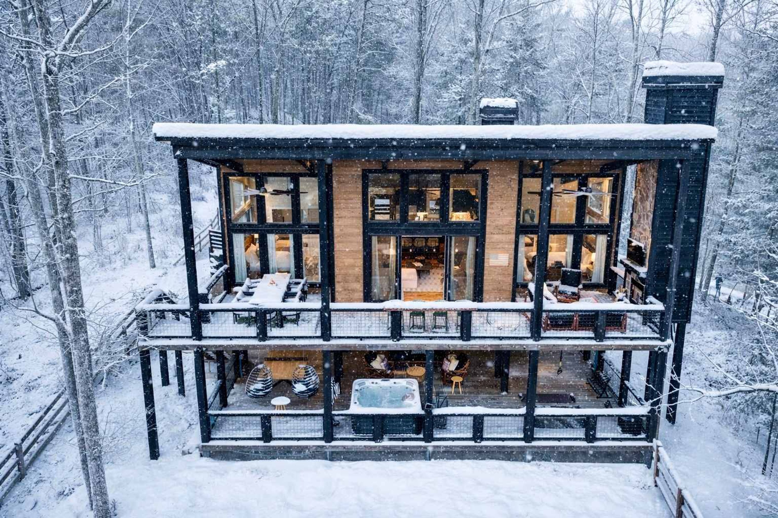Een houten chalet met twee verdiepingen, grote ramen, een balkon en een besneeuwde buitenkant.