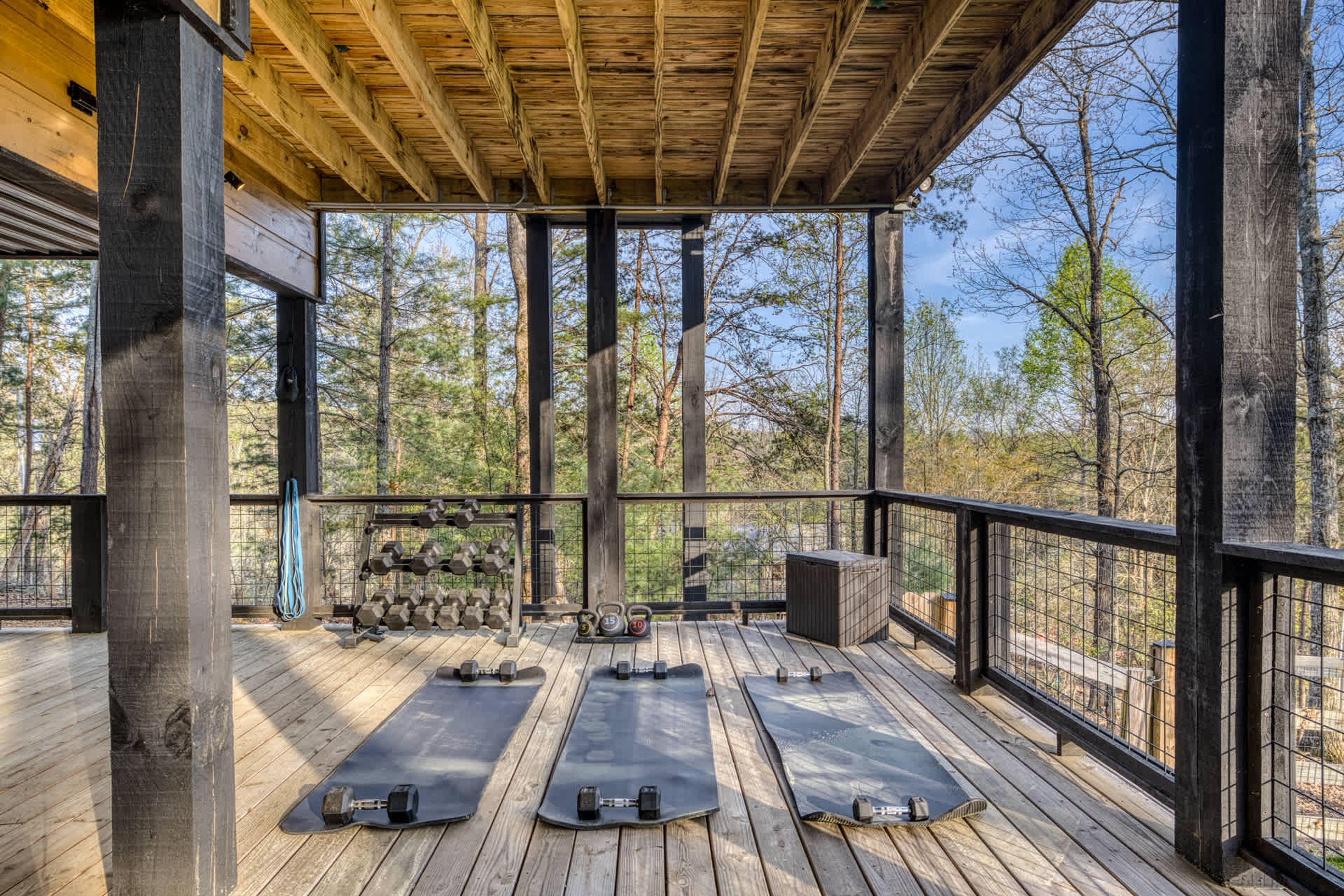 A covered outdoor deck with exercise equipment, including dumbbells and kettlebells, and a trash bin.