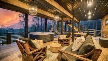 A wooden deck with outdoor seating, a hot tub, and a view of the surrounding forest.