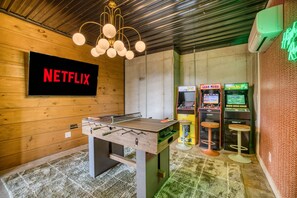 Een kamer met een tafelvoetbaltafel, een Netflix-bord en speelautomaten.