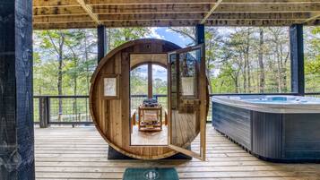 Un bain à remous en bois, installé dans une structure circulaire également en bois, avec vue sur une forêt.