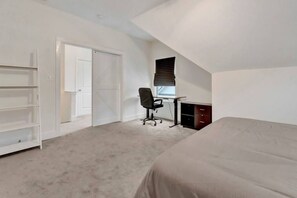 Ein Schlafzimmer mit Bett, Schreibtisch, Stuhl, Kleiderschrank und einer Tür.