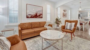 Ein geräumiges Wohnzimmer mit einem braunen Ledersofa, einem Marmortisch und einem Holzschaukelstuhl.