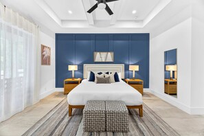 A modern bedroom with a large bed, two bedside tables with lamps, a ceiling fan, and a large mirror on the wall. - Marco Island Escape Pool Game Room (Marco Island)